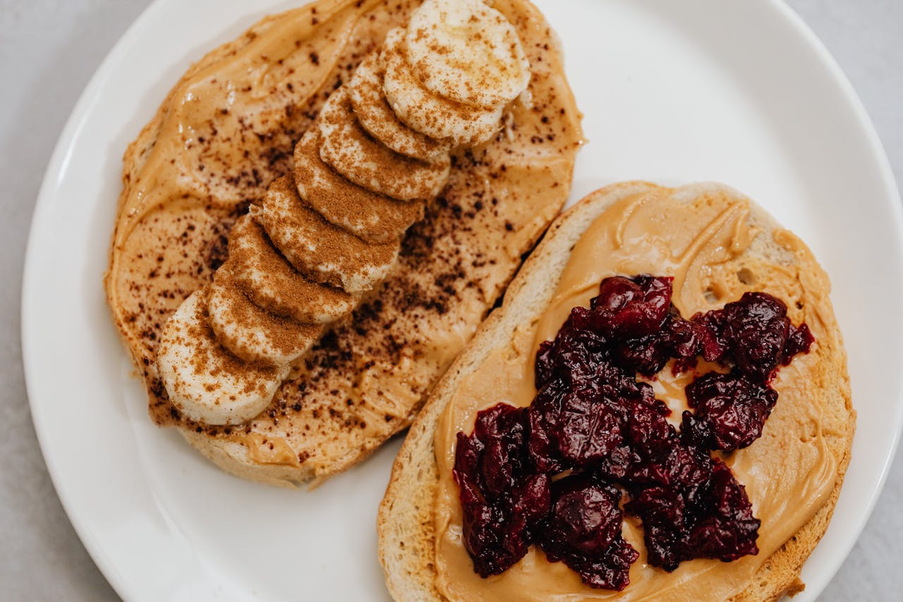 services-05 Close-up of peanut butter toast with banana and jam toppings on a plate.